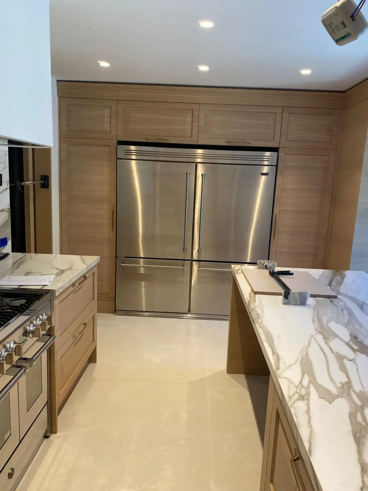 Fitted kitchen in timber veneer with integrated stainless appliances and a marble-topped island